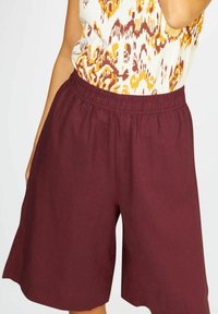 Bordové šortky s elastickým pasem, vyrobené z lehkého materiálu. Design má volný střih a sahá těsně nad kolena.
