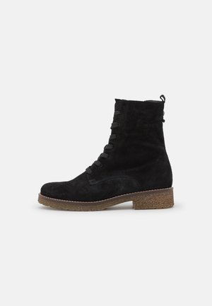 Schwarze Wildleder-Ankle-Boots mit runder Zehenform, Schnürung vorne, strukturiertem Absatz und kontrastierender Sohle. Verfügt über eine Schlaufe an der Rückseite für einfachen Einstieg.