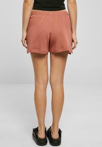 Růžové bavlněné šortky s elastickým pasem, mají volný střih a mírně zaoblený lem. Nosené s černou obuví.