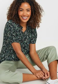 Blusa negra con flores y mangas cortas, que presenta flores verdes y blancas. Combinada con pantalones cortos de color verde claro y zapatillas blancas.