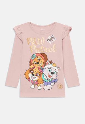 Ružová košeľa s dlhými rukávmi, na ktorej sú zobrazené tri karikatúry psov zo "Paw Patrol" so trblietavým textom a volánovými rukávmi. Vyrobená z mäkkej bavlny.