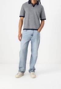 Polo de manga corta en patrón geométrico azul marino y blanco, combinado con jeans rectos de color azul claro y zapatillas crema. Ajuste relajado, estilo casual.