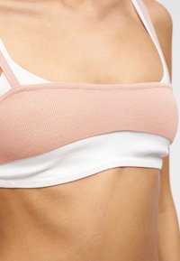 Κοντινή λήψη του κορμού που φοράει μια ροζ ριγωτή crop top σε στρώσεις πάνω από ένα λευκό αμάνικο ένδυμα.