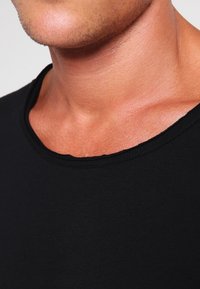 Camiseta negra de manga corta con un escote ancho y acanalado, hecha de material de algodón suave, con una textura lisa y un diseño ajustado.