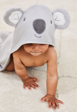 Baby kravler på tæppe iført gråt hættede håndklæde med koalaansigt og ører.