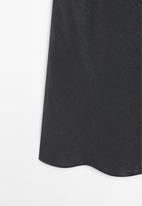 Černá látková sukně s hladkým, mírně strukturovaným povrchem a zvlněným lemem, odrážející jemné variace světla.