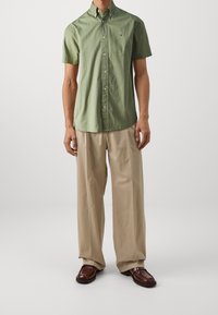 Korte mouwen, lichtgroen overhemd met knopen van katoen met een klein logo. Gecombineerd met beige, loszittende broeken en bruine instappers.