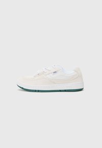 Beige nubukist sneakers valgete aktsentidega, ümmarguse kujuga ja rohelise kummitaldaga. Omab paelu ja külge logodetaili.