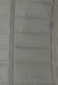 Grå vadderad väst med en framdragkedja, med en slät yta och subtil branding. Lättviktigt material utformat för isolering.