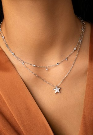 Collane d'argento a strati con piccoli accenti rotondi e a goccia, e un pendant a stella prominente sulla catena inferiore.