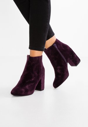 Paarse suède enkellaarsjes met blokhak, voorzien van een ritssluiting en een gladde textuur. Gecombineerd met zwarte strakke jeans.