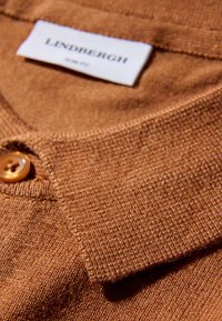 Ruskea neulottu poolopaita, jossa on teksturoidun näköinen kangas, teräväkaulus ja pyöreä napitus. Merkki näkyy pääntiellä.