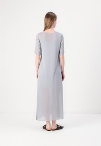 Robe maxi légère gris clair, en voile, avec des manches courtes, un col rond et des fentes latérales, présentant une texture lisse et un design minimaliste.