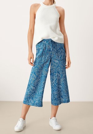 Lehké modré zkrácené kalhoty s listovým vzorem, spojené s bílým žebrovaným tílkem bez rukávů a bílými teniskami.