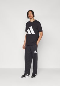 Sort bomuld t-shirt med et stort hvidt Adidas-logo, parret med sorte sweatpants med et mindre hvidt logo på låret. Sorte sportssko.