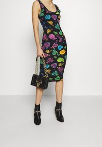 Sukienka bodycon w kolorze czarnym z kolorowymi zawijasami i wzorami. Połączona z czarnymi botkami za kostkę i czarną torebką na łańcuszku w złotym kolorze.