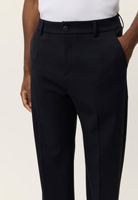 Μαύρο παντελόνι με ίσια γραμμή, πλαϊνές τσέπες και κλείσιμο με κουμπί. Κατασκευασμένο από λείο ύφασμα, με εφαρμοστή γραμμή και ραφή στην πρέσα.