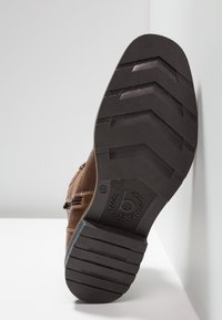 Scarpa in pelle marrone con suola in gomma nera testurizzata caratterizzata da un motivo a zigzag, logo impresso e dettagli di cucitura laterale.