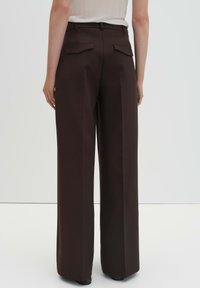 Pantaloni marroni a gamba larga con vita alta, dotati di due tasche posteriori e design sartoriale. Il tessuto appare liscio e strutturato.