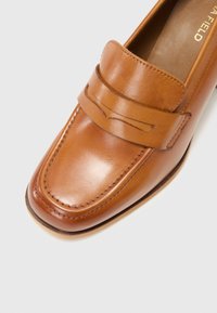 Brune lær loafers med en glat overflade, der har en struktureret tå, forhøjede syninger og et dekorativt bånd hen over vampen.