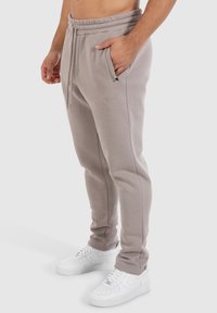 Grijze trainingsbroek met een elastische tailleband, zijzakken en een klein logo op de dij. Gecombineerd met witte sneakers. Soepele textuur.