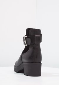 Czarne botki sięgające kostki z zaokrąglonym noskiem, górą o teksturowanej skórze i srebrną klamrą na pasku wokół kostki. Gruby, masywny obcas.
