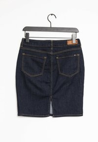 Mörkblå denimkjol med bakfickor, gul sömnad, en liten flaggetikett på höger ficka och en slits i mitten bak, hängande på en svart galge.