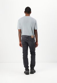 Camiseta gris de manga corta, combinada con unos vaqueros gris oscuro con bolsillos traseros y una etiqueta de parche. Footwear negro completa el conjunto.