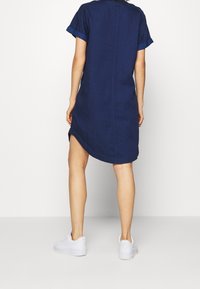 Marineblauw kortgehandd dress met een rechte snit, voorzien van een iets langere achterkant en opgerolde mouwmanchetten, gemaakt van een textuurt stof.