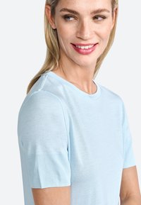 Hele sinine lühikeste varrukatega särk, mis on valmistatud pehmest kangast ning millel on klassikaline ümmargune kaelus. Sile tekstuur ja ribakujuline aktsent varrukatel.