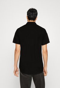 Chemise noire à manches courtes, en coton, col classique, coupe droite, texture lisse, avec un empiècement et des coutures sur les épaules.