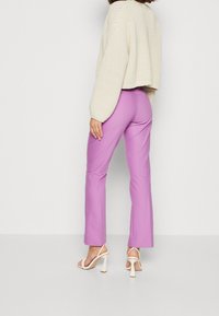 Pull en tricot léger et court, couleur crème. Pantalons taille haute ajustés en lavande vif. Sandales blanches à bouts ouverts avec talons blocs.