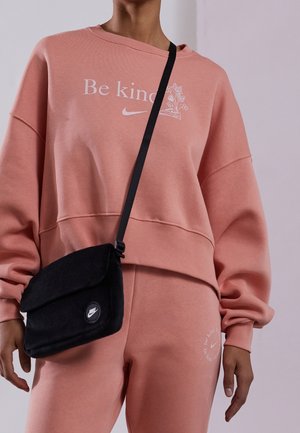 Felpa corta rosa con testo e grafiche bianche, abbinata a pantaloni coordinati. Una borsa a tracolla nera presenta un logo circolare.