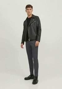 Black leather biker jacket with zippers, black t-shirt, gray slim-fit trousers, and black shoes. Model stands on a light background.