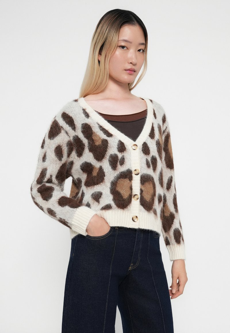 Kardiagan w panterkę w kolorze kremowym i brązowym, z dekoltem w kształcie litery V, ściągaczami na rękawach oraz pięcioma złotymi guzikami z przodu. Teksturowany materiał dzianinowy.