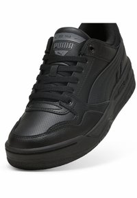 Zapatillas de cuero negro con punta texturizada, collar acolchado y cordones planos. Logotipo en la lengüeta y en el costado, suela de goma con tracción.