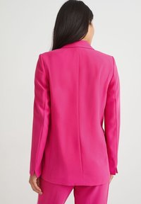 Blazer rosa aderente realizzato in tessuto liscio, con un'unica spaccatura sul retro e revers affilati, stile con maniche su misura.