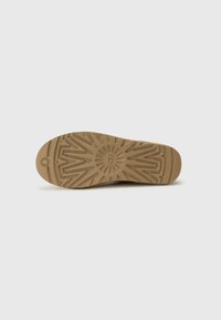 Suola di scarpa in gomma marrone con un motivo di battistrada dettagliato, che include scanalature e un logo circolare, su uno sfondo bianco semplice.