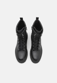 Bottines en cuir noir avec une finition lisse, un design à lacets et une fermeture éclair sur le côté. Elles disposent d'une semelle robuste et d'œillets en métal pour les lacets.