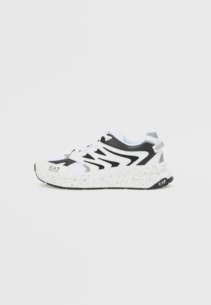 Zapatilla deportiva blanca y negra con suela gruesa moteada y marca EA7 en las zonas del dedo y del talón, mostrada de perfil.
