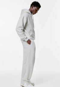 Lichtgrijze hoodie en sweats gemaakt van zachte stof. De hoodie heeft een voorvak, terwijl de sweatpants zijzakken en een relaxed fit hebben.