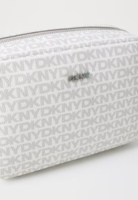 Borsa cosmetica bianca texturizzata con motivo ripetuto "DKNY" e placca in argento. Presenta una chiusura con zip. Dimensioni non specificate.
