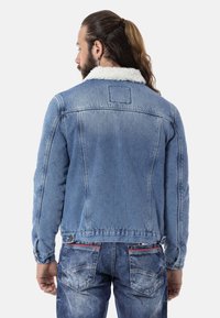 Denimjacke mit Sherpa-Kragen, hellblaue Farbe, taillierter Schnitt, dezente Verwaschungen und Knopfdetails an den Ärmeln und am Saum.