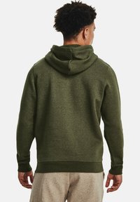 Grøn bomulds-hoodie med rund hætte, tekstureret stof, manchetter ved ærmerne og ribbet kant, båret med lyse bukser.