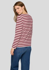 Langärmliges Oberteil mit roten und cremefarbenen Streifen und einem Rundhalsausschnitt, kombiniert mit blauen Denim-Jeans. Verfügt über eine entspannte Passform und glatten Stoff.