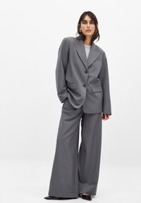 Grå pinstribet jakkesæt med en oversized jakke med store revers og vide bukser. Fuldsat med sort fodtøj for kontrast.