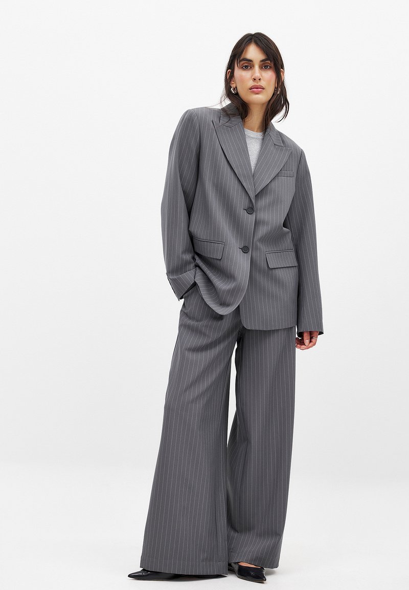 Grå pinstribet jakkesæt med en oversized jakke med store revers og vide bukser. Fuldsat med sort fodtøj for kontrast.