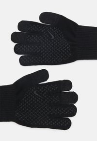 Les gants en tricot noirs présentent un motif de grip texturé sur les paumes et les doigts, avec des poignets côtelés et un accent logo subtil.