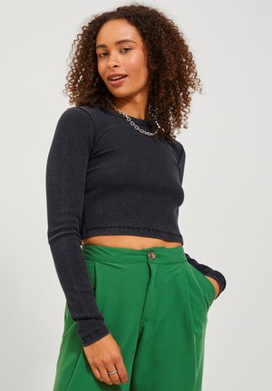 Zwarte geribbelde langemouwen crop top, gecombineerd met hoge groene broeken. Opvallende details zijn de ronde halslijn en de getailleerde pasvorm.