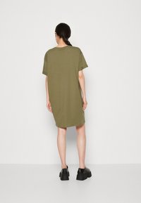 Oliwkowa, krótko rękawowa sukienka koszulowa do kolan. Miękki materiał w luźnym kroju. Noszona z masywnymi czarnymi butami. Minimalistyczny design.